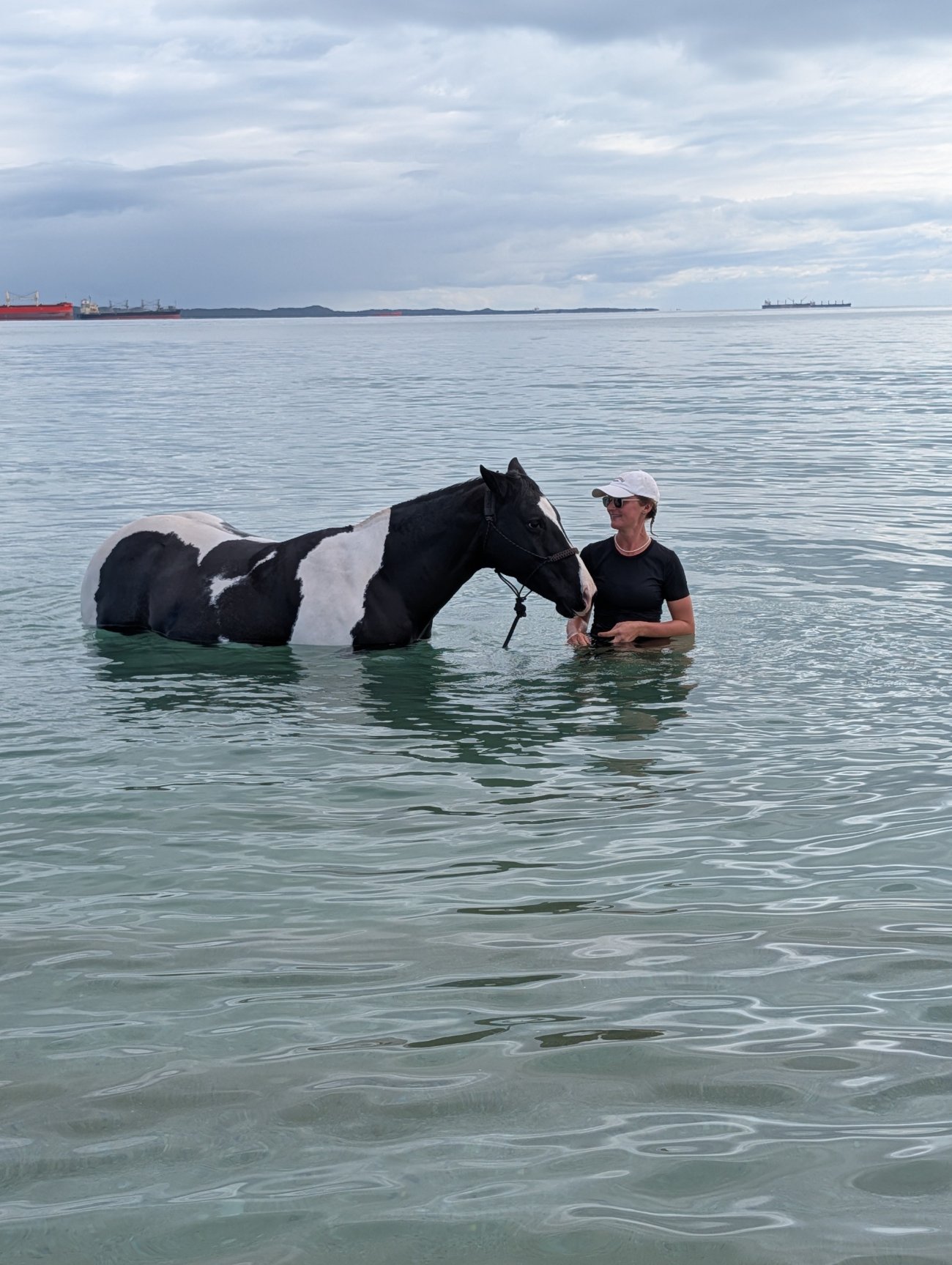 Brooke standing in the ocean alongside her black and white horse